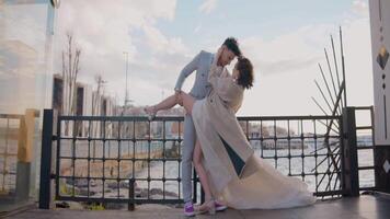 Newlyweds on background of pier. Action. Beautiful newlyweds pose between city buildings. Stylish newlyweds hug on background of city pier in cloudy weather video