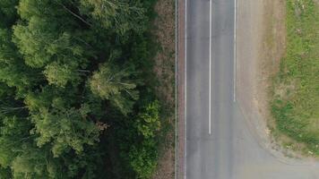 visie van een helikopter . tafereel . een versmallen weg Aan welke een lading vrachtauto met een blauw voorkant en een auto met een aanhangwagen voor vervoer zijn op reis , Daar is een Woud en een weg met gras dichtbij . video