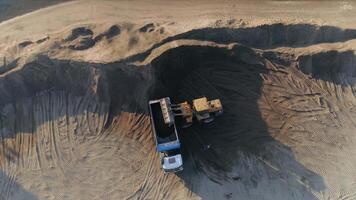 sand brytning industri, sand mina på de stenbrott. scen. antenn topp se av en bulldozer maskin sätta sand till de lastbil kropp. video