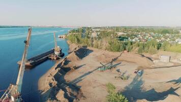 Construction cranes and trucks on shore. Scene. Top view of clearing of construction site on lake shore. Start of construction on lake shore on sunny day video