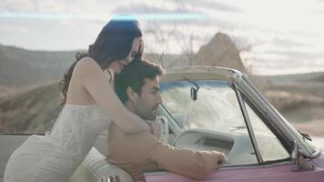 An interesting beautiful photo shoot of the newlyweds. Action. The bride of pretty appearance in a narrow beautiful white long dress with her cute groom in a brown suit are photographed posing next to video