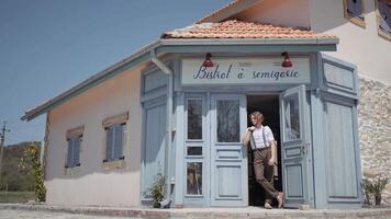 Caucasian male standing near entrance of the small cafe under the hot summer sunlight. Action. Young man with curly hair by the door of cute bistro. video