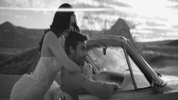 Beautiful couple in convertible. Action. Stylish newlyweds pose in convertible. Beautiful couple in love in car on background of canyon. Black and white shooting video