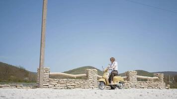 Summer landscape with a man. Action. A handsome man with long hair on a small green motorcycle on a beautiful landscape with blue sky and mountains. video