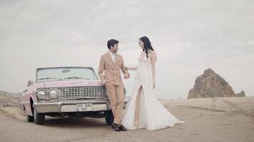 Beautiful young couple during photo session on the top of a mountain in Cappadocia. Action. Romantic love of man and woman couple near the cabriolet pink car. video