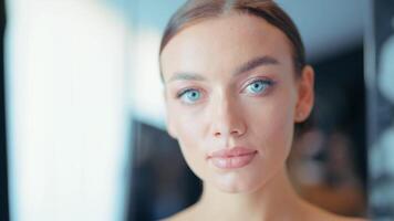 Beautiful face of tender attractive brunette woman with blue eyes staying indoors on dark blurred background. Action. Close up of confident young lady posing in front of a camera. video