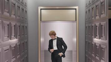 hermoso elegante novio en el hotel interior posando en frente de el cámara. acción. hombre en negro traje y blanco camisa en pie por el pared en el final de el corredor. video