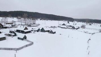 Nevado ojo de pájaro vista. acortar. un blanco pueblo en el nieve con pequeño de madera casas y siguiente a eso un grande bosque con alto arboles video