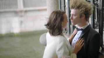 Passionate bride and groom embracing by the iron gate. Action. Sexy young man and woman in suit and white dress in windy weather. video