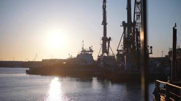 Ships standing right under the rays of the bright sun.Clip. Large ships in the river with large cargo devices stand against the background of the bright sun during the day. video