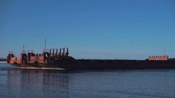 Cargo ship sailing on river on clear day. Clip. Merchant ship or barge sails along river. Commercial and industrial shipping video