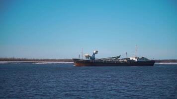 Cargo ship sailing on river on clear day. Clip. Merchant ship or barge sails along river. Commercial and industrial shipping video