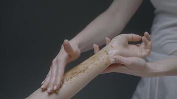 Applying body sugar scrub on female client arm, concept of body care. Action. Close up of female cosmetologist hand during beauty procedure at the salon. video