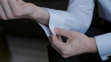 The man gets dressed and does his buttons on the sleeves of his white shirt. Action. Close up of male arms, man sitting and trying to button up. video