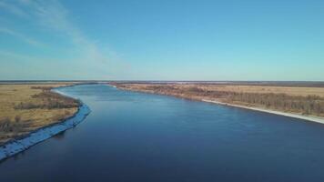 Top view of beautiful blue river on background of fields and sky. Clip. Beautiful panorama of river stretching away to horizon with blue sky. Blue river among yellow fields video