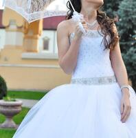 Close-up portrait of young beautiful bride in a wedding dress standing on a green field and holding a white umbrella photo