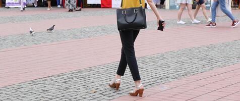 mujer vistiendo un negro bolso y participación un inteligente teléfono en su mano es caminando en el vista de calle desde el espalda foto