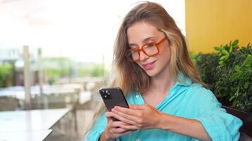 lächelnd Frau im Blau Hemd mit Smartphone beim Cafe Terrasse video