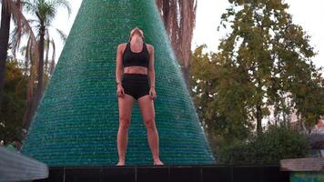 vrouw atleet in sportkleding aan het doen warm omhoog oefening in de buurt fontein in park video