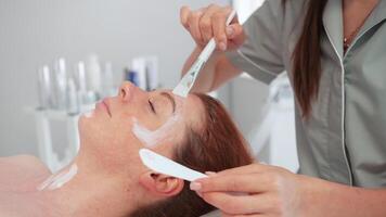 cosmetólogo aplicando cara peladura máscara a relajado joven mujer a spa video