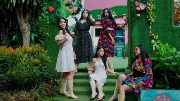 Group of diverse women posing in a lush garden setting with vibrant greenery and colorful dresses. video