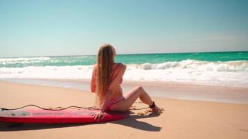 vrouw surfer resting Aan surfboard glimlachen in de buurt zee Aan zanderig strand video