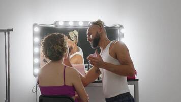 gay homme avec tatouage appliquant maquillage sur femme dans studio arrière vue video