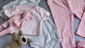 Set of baby bodysuits, pants, socks and knitted toy on grey background. video
