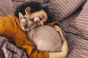 un joven niño duerme pacíficamente, abrazando un sin pelo sphynx gato foto