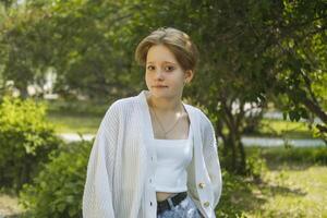 Close-up portrait of a red-haired teenage girl in the park against the backdrop of foliage. photo