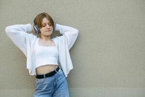 Portrait of a teenage girl in headphones against a gray wall. photo