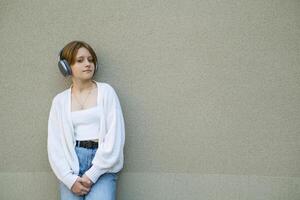 retrato de un Adolescente niña en auriculares en contra un gris pared. foto