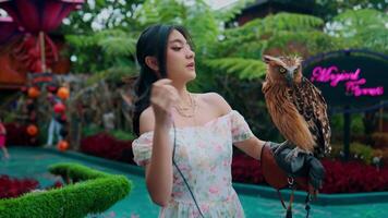 jovem mulher segurando uma majestoso coruja dentro uma exuberante jardim contexto. video