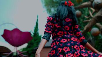 Rear view of a woman in a floral dress standing under a tree with vibrant foliage, evoking a sense of mystery and nature. video