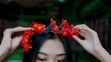 Close-up of a person adjusting a red floral headband with a blurred green background. video