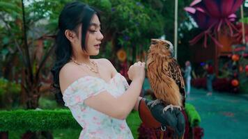 retrato do uma jovem mulher segurando uma Castanho coruja dentro uma exuberante jardim contexto. video