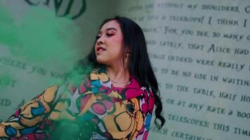 Woman in colorful outfit posing with a green smoke bomb, with graffiti wall background. video