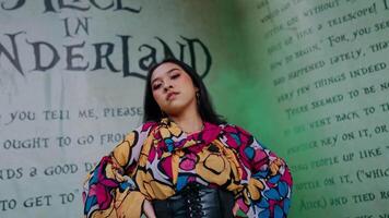 Fashionable woman posing in front of a graffiti wall with wonderland theme, wearing a colorful dress and boots. video