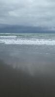 charmant Strand Wellen erhebt euch und fallen sanft auf das Ufer, mit schaumig Spitzen und teilweise wolkig Himmel durch das Meer, und leicht braun Sand video