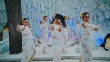 Blurred image of people in white costumes dancing, with a whimsical winter backdrop and penguin figures. video