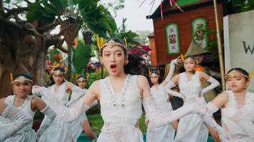 Group of young dancers in white costumes performing traditional dance outdoors with greenery in the background. video