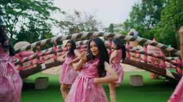 Group of women in pink dresses dancing under a braided archway in a garden setting. video