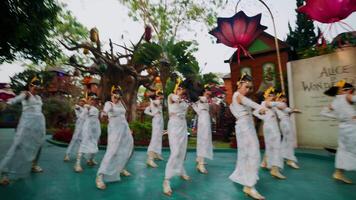 Traditional dancers in white costumes performing outdoors with large floral decorations in the background. video