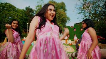 Two women in traditional pink dresses enjoying a sunny day at an outdoor park setting. video