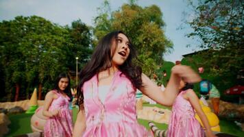 Joyful young women in pink dresses dancing in a sunny park setting. video