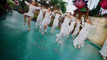 Group of dancers in white performing outdoors with large floral decorations in the background. video