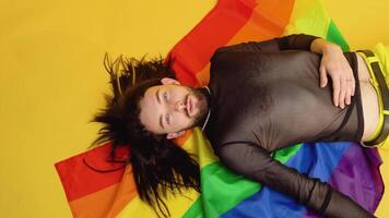 jung kaukasisch Fröhlich Mann mit Regenbogen gestreift Flagge Lügen auf Gelb Hintergrund. Menschen Lebensstil Mode lgbtq Konzept video