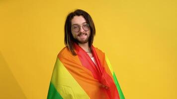 joven activista sonriente contento gay hombre sostener arco iris bandera aislado en amarillo antecedentes estudio. personas lgbt estilo de vida concepto video