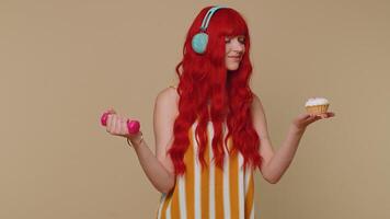 Redhead young woman hold dumbbell and sweet donut cake choosing between fitness diet or junk food video