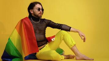 Young caucasian gay man 20s with rainbow striped flag sits on yellow background. People lifestyle fashion lgbtq concept video